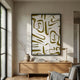 Dunari Olive Trace III Wood Carving 3D Wall Art with olive cut-outs on textured white in a black frame, above an oak sideboard with vase and books.