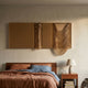 Drapelle Gold Flow Layered Leather 3D Wall Art by Giant Sculptures mounted above a wooden bed with rust and blue linens, beside a nightstand and lamp.