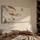 Scalora Copper Fragmented Leather 3D Wall Art mounted above a bed dressed in tan linen, beside a globe lamp and wooden bookshelf in a warm bedroom.