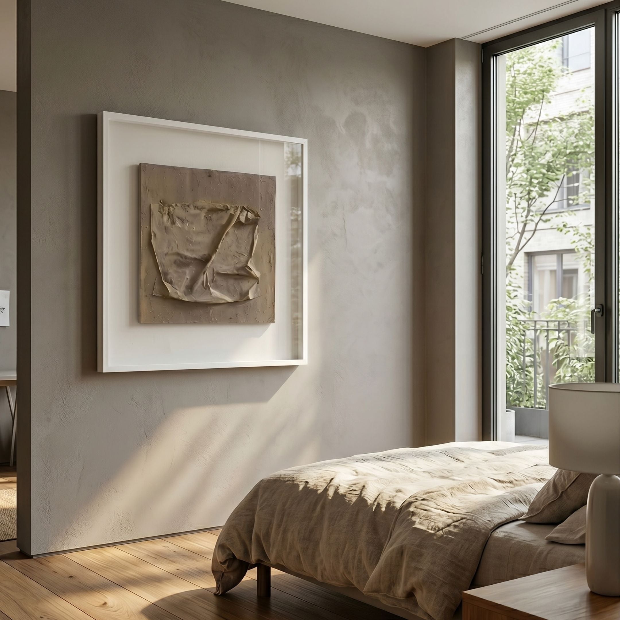 Crustara Folded Earth Hand Painted Wall Art by Giant Sculptures, a beige folded-fabric square in a white frame, displayed above a linen bed in a sunlit bedroom.
