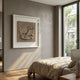 Crustara Folded Earth Hand Painted Wall Art by Giant Sculptures, a beige folded-fabric square in a white frame, displayed above a linen bed in a sunlit bedroom.