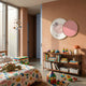 Blossomkin Pink Petal Bird Kids 3D Wall Art by Giant Sculptures, two gold-rimmed overlapping discs on a terracotta wall above a child's bookshelf and toys.