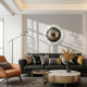 A modern living room has a gray sofa with metallic and gold pillows, an orange armchair, a marble coffee table, and a floor lamp. Above the couch is Giant Sculptures’ Iriselle Amber Flare Crystal Porcelain 3D Wall Art; dried flowers decorate the table.