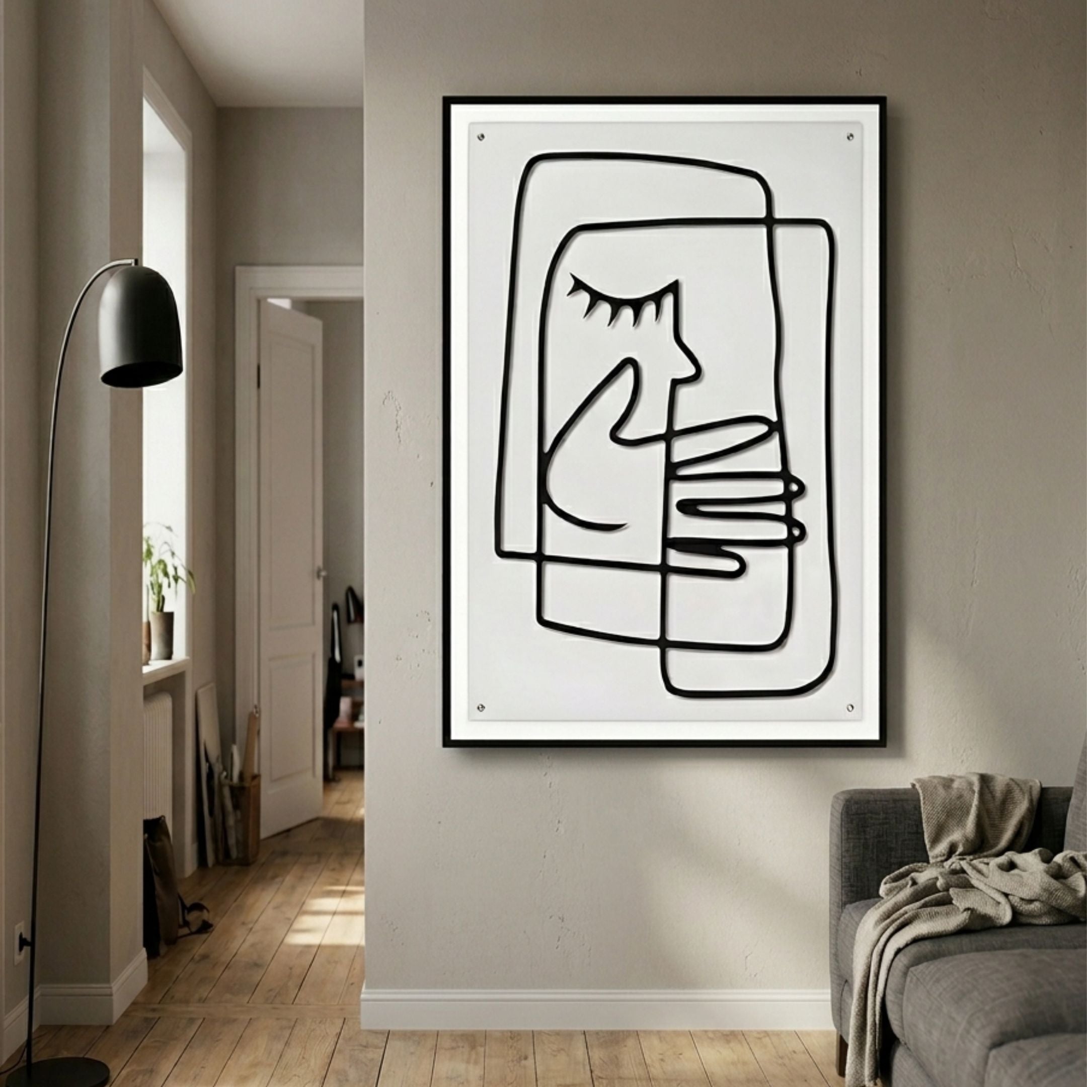 Linea Gentle Profile Minimal Acrylic UV 3D Wall Art with continuous black line face and clasped hands, framed on a hallway wall beside a floor lamp and grey sofa.