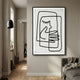 Linea Gentle Profile Minimal Acrylic UV 3D Wall Art with continuous black line face and clasped hands, framed on a hallway wall beside a floor lamp and grey sofa.