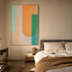 Bounce Orange & Mint Panel Acrylic 3D Wall Art in a gold frame, displayed above a wooden nightstand beside a bed with cream linens in a warm bedroom.