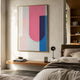Bounce Pink & Blue Panel Acrylic 3D Wall Art by Giant Sculptures in a gold frame, displayed above a floating wood shelf beside a bed in a sunlit bedroom.