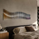 Waveline Amber & Plum Gradient Wave Acrylic 3D Wall Art mounted above a dark upholstered headboard in a bedroom with linen bedding and a wooden nightstand.