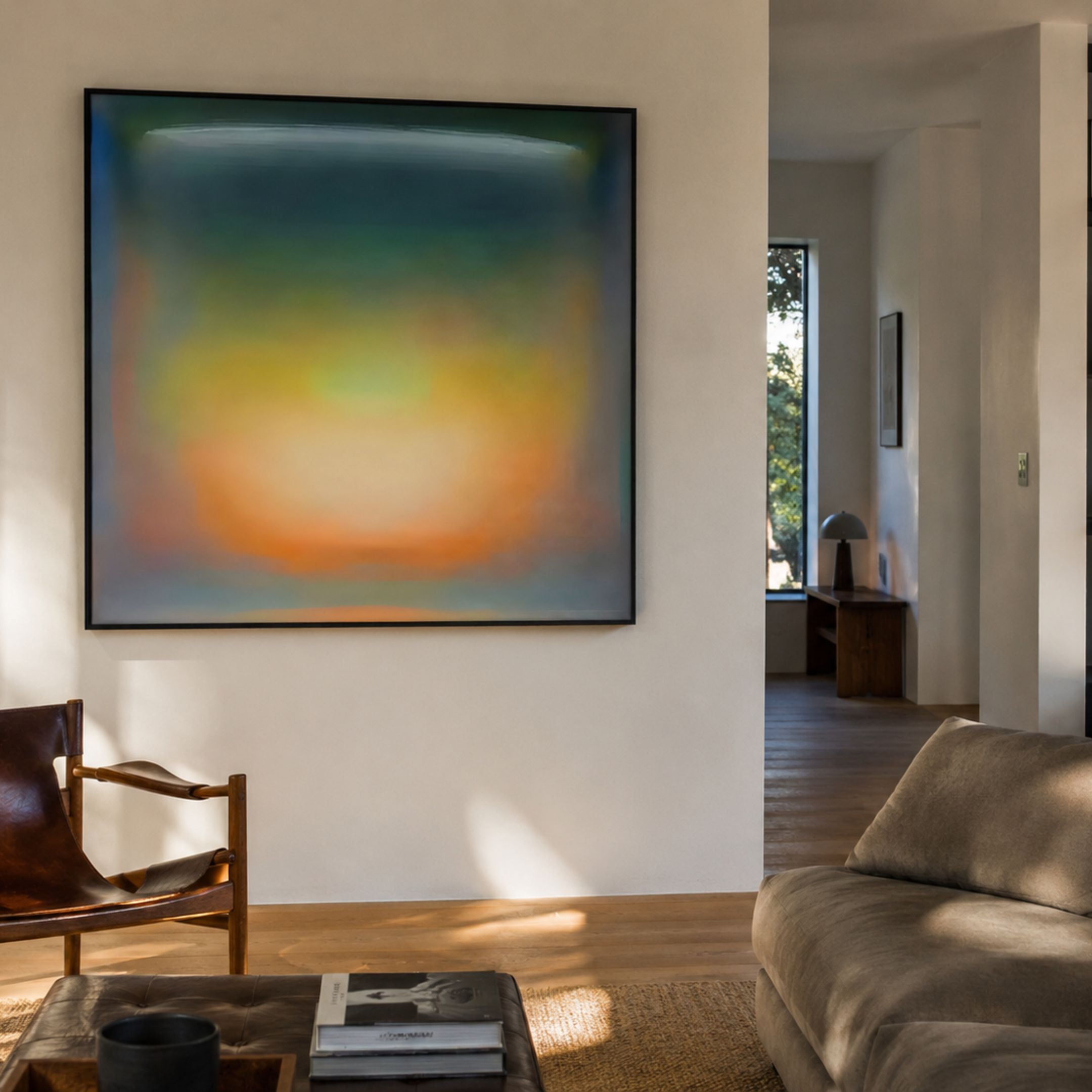 Lumin Ambient Glow Illusion Crystal Porcelain Wall Art by Giant Sculptures displaying a teal-to-amber gradient in a slim black frame above a leather chair.