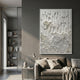 Tessara Ivory Organic Drape Felt 3D Wall Art displayed above a taupe sofa in a modern grey living room with bookshelf and side table.