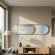 Modvara Sky Blue Fusion Acrylic & Leather Wall Art displayed above a light oak console in a modern living room, pairing a gold-framed oval panel with a blue circle.