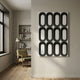 Revela White & Black Geometric Wood Relief 3D Wall Art with twelve black ovals on a light panel, mounted in a modern room with a green armchair.