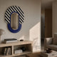 Arcus Purple & Black-White Striped Mirror 3D Wooden Wall Art mounted above a wooden console with books and a lamp in a neutral-toned living room.