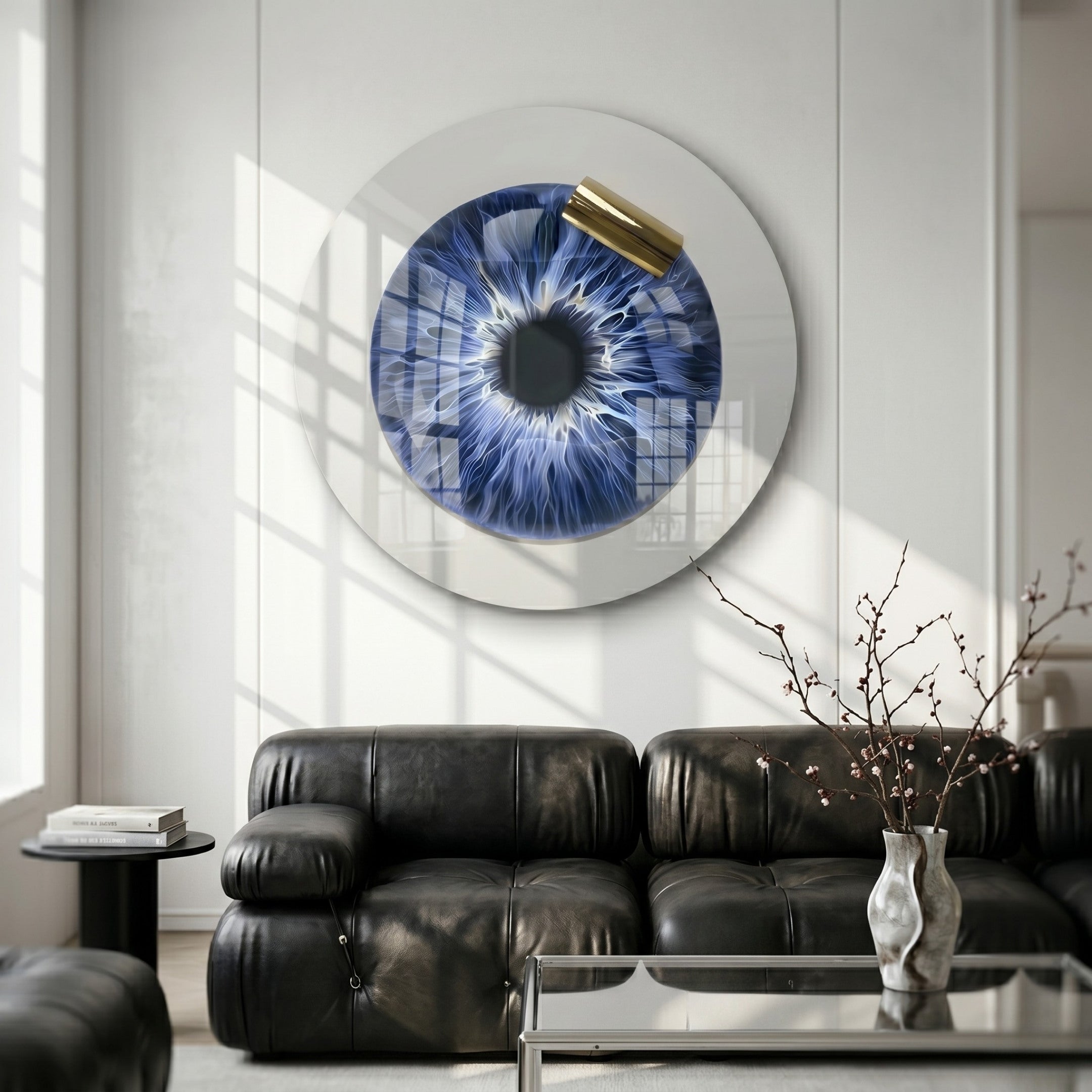 A modern living room with black leather sofas, a minimalist coffee table, and the Giant Sculptures Iriselle Sapphire Iris Crystal Porcelain Round 3D Wall Art featuring an eye-like design with gold accents. A vase of thin branches adds elegance.