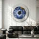 A modern living room with black leather sofas, a minimalist coffee table, and the Giant Sculptures Iriselle Sapphire Iris Crystal Porcelain Round 3D Wall Art featuring an eye-like design with gold accents. A vase of thin branches adds elegance.