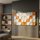 Averra White & Orange Geometric Wood Relief 3D Wall Art by Giant Sculptures, mounted on a grey living room wall beside a wooden bookshelf and grey sofa.
