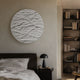 Orenda Ripple Wave White Wood Relief 3D Wall Art mounted above a brown bed and black lamp, with a tall bookshelf in the adjoining nook.