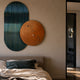Embera Abstract Circle Teal Ombre 3D Wall Art by Giant Sculptures, with a ribbed teal oval and bronze disc, mounted above a bed in a modern bedroom.