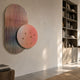 Embera Abstract Circle Warm Blush Gradient 3D Wall Art mounted in a modern living room, featuring a striped oval and blush circle with gold spheres beside a bookshelf.