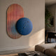Embera Abstract Circle Multicolour Gradient 3D Wall Art with blue rippled disc over a pink-to-blue striped oval, displayed in a modern living room.