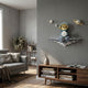 Blue 3D Dreamer Glow Astronaut Wall Art by Giant Sculptures, mounted on a grey living room wall above a walnut console with books, beside a grey sofa.