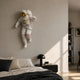 White 3D Cosmic Lift Astronaut Wall Art by Giant Sculptures mounted above a bed, mid-lift pose with gold visor and red accents, beside a black nightstand.