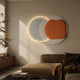 Arcadia Terra Amber Leather 3D LED Wall Art by Giant Sculptures, with overlapping white and amber circles and a glowing LED ring, above a beige sofa.
