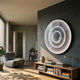 Reflex Silver Mirror LED 3D Wall Art by Giant Sculptures mounted on a charcoal wall above a wooden console in a modern living room with a grey lounge chair.
