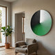 Orbit Emerald Hand-Painted Canvas 3D LED Wall Art by Giant Sculptures, circular piece with emerald, white, and black blended fields, mounted in a living room above an armchair beside a fiddle leaf fig.