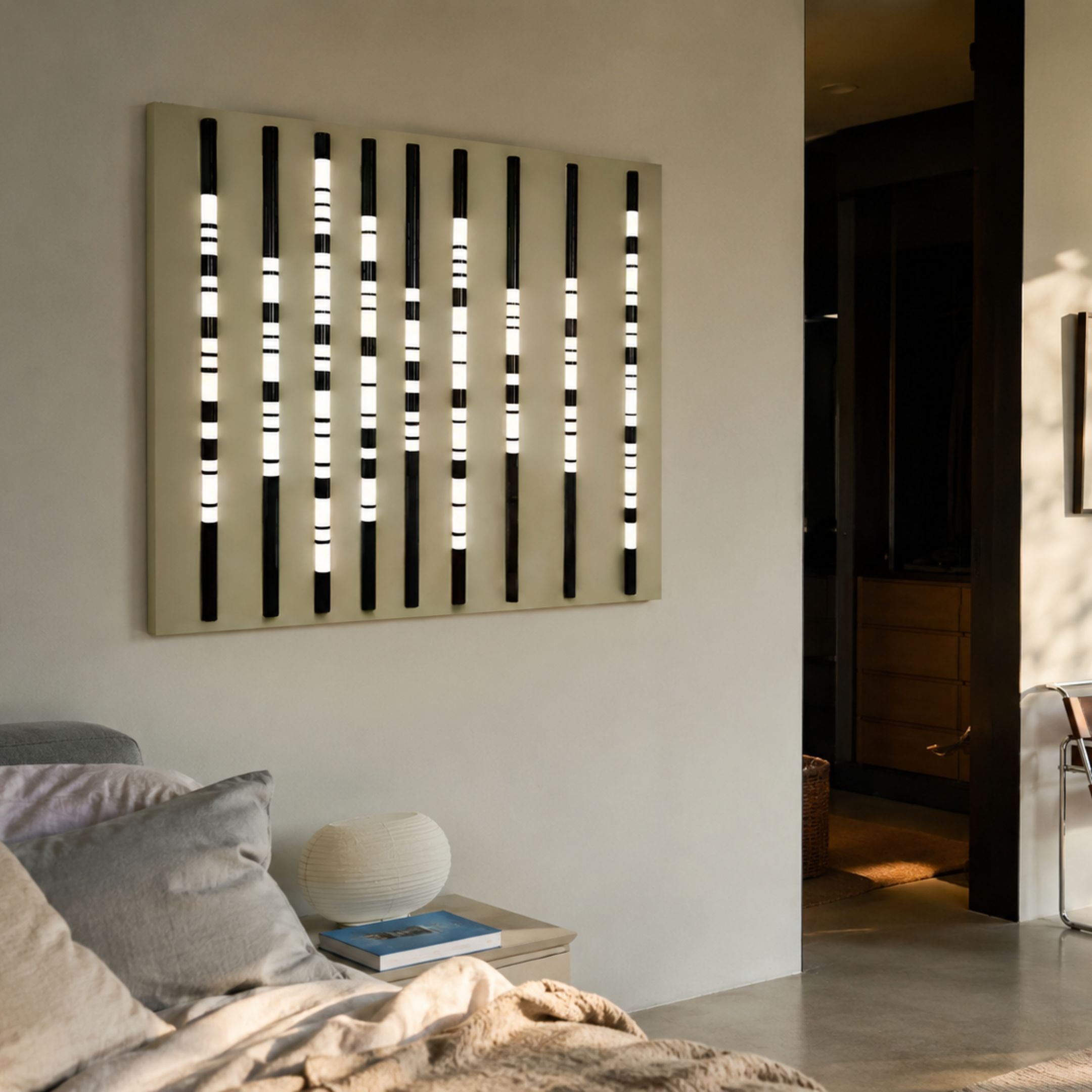 Strata Slate LED Wall Art by Giant Sculptures mounted above a side table in a neutral living room, its vertical black rods glowing with white striped segments.