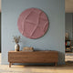 Orbura Blush Pink Circular 3D Wood Relief Wall Art by Giant Sculptures mounted on a soft blue wall above a walnut sideboard with a vase and books.