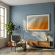 Elytrum Orange Grid Gradient Hand-Painted Wood Relief 3D Wall Art in a black frame mounted on a blue wall above a wooden sideboard, beside a grey armchair and fiddle-leaf fig.