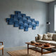 Axura Blue Geometric Wood Relief 3D Wall Art mounted above a linen sofa and wooden coffee table in a grey-walled living room with a floor lamp.