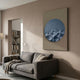 Solivis Ocean 3D Wood Relief Wall Art by Giant Sculptures, a blue wave-textured disc on beige canvas, displayed above a grey sofa in a modern living room.