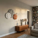 Orbita 4-Set Circular Sand & Rust 3D Wood Relief Wall Art by Giant Sculptures displayed above a walnut sideboard in a sunlit living room with bookshelves.