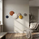 Orbita 6-Set Circular Earth-Tone 3D Wood Relief Wall Art by Giant Sculptures arranged in a cluster of navy, brown, white, beige, yellow, and grey discs above a linen-draped chair.