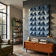 Ondula Textured Blue Wood Relief 3D Wall Art by Giant Sculptures mounted on a grey wall above a teak sideboard in a modern living room with bookshelf.