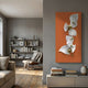 Aurelia Orange & White 3D Wood Wall Art With Metal Ball by Giant Sculptures displayed on a grey wall in a modern living room with bookshelf and armchair.