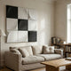 Curvatura White & Black Grid 3D Wood Relief Wall Art by Giant Sculptures mounted above a beige linen sofa in a living room with a bookshelf and floor lamp.