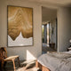 Celoria Golden Dune Wood Carving 3D Wall Art with carved wavy golden-brown ridges, displayed on a cream bedroom wall beside a linen bed and wooden chair.