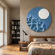 Verve Soft Blue Wood Relief 3D Wall Art by Giant Sculptures, a round blue carved disc with white moon, mounted above a wooden bed beside a black bookshelf.