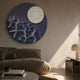 Verve Soft Purple Wood Relief 3D Wall Art by Giant Sculptures, a round bluish-purple panel with a raised white disc, displayed above an olive sofa in a sunlit living room.