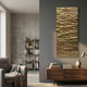 Illume Gold III Hand-Painted Wood Relief 3D Wall Art mounted on a grey wall in a modern living room with a wooden sideboard, books, and grey armchair.