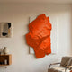 Veritas White & Orange Wood Relief 3D Wall Art by Giant Sculptures displayed in a living room above a wooden shelf with a vase, beside an armchair.