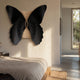 Lucerna Black Butterfly Wood Carving 3D Wall Art by Giant Sculptures displayed above a wooden bed in a sunlit modern bedroom with beige walls.