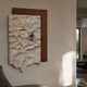 Calidora Terra Sculpted Textured 3D Relief Wall Art with a brown base, draped white sheet, and silver sphere, mounted on a neutral wall in a modern living space.