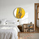 A cozy bedroom with a neatly made bed in white linens, the Auralune Citrine Column Abstract Round 3D Wall Art by Giant Sculptures, a brass lamp, bookshelf with books and ceramic pot, and sunlight streaming through the window.