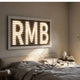 Aurova II Contemporary Glow 3D LED Wall Art by Giant Sculptures with illuminated white RMB letterforms on a slatted grey panel above a bedroom headboard.