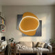 Gleam Amber Glow 3D Leather LED Wall Art by Giant Sculptures, an amber organic form with white-lit outline over dark grey panels, above a beige sofa.