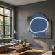 Gleam Azure Elegance 3D Leather LED Wall Art mounted above a grey sofa and wooden coffee table, its azure form glowing with a curved LED line against dark panels.